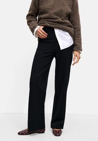 Black wide-leg trousers paired with a brown textured sweater over a white collared shirt. Burgundy studded flats complete the outfit.
