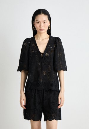 Svart bluse i øyelet med korte pufferm og V-hals, med en scalloped kant og blondedetaljer, kombinert med matchende shorts.