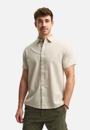 Kortærmet skjorte med krave i struktureret lys beige stof med knapper foran. Parret med olivengrønne cargo shorts, minimale hardware detaljer.