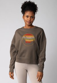 Olijfgroene sweatshirt met een ronde, veelkleurige zonsonderganggrafiek en bossilhouetten. Beschikt over een relaxed fit en ribbels aan de mouwen.