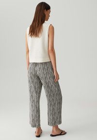 Crème gebreide mouwloze top gecombineerd met zwart-witte wijde broek met een bladpatroon. Platte sandalen maken de outfit compleet.