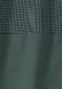 Grüner Stoff mit einem strukturierten Rastermuster im oberen Bereich und einer glatten, matten Oberfläche im unteren Bereich.