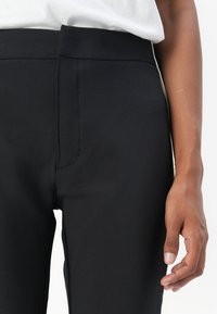 Black tailored pants with a smooth texture, featuring a high waistband and front seam detail. Minimalistic design, suitable for various occasions.