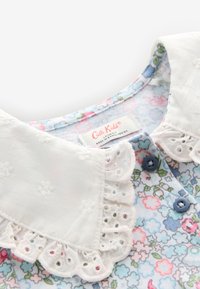 Bluse mit Blumenmuster, die einen weißen, bestickten Kragen mit Spitzenbesatz, blaue Knöpfe und ein Pflegeetikett in der Nähe des Halsausschnitts aufweist.