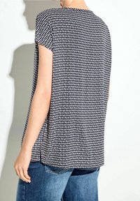 Top a maniche corte bianco e nero con un motivo a righe, dalla vestibilità ampia e con spacchi laterali, realizzato in tessuto leggero. Indossato con jeans blu.