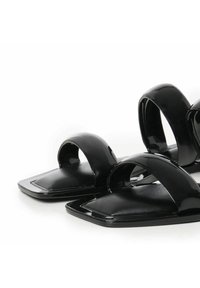 Sandales en cuir verni noir avec de larges brides courbées, un bout carré plat et une texture lisse, dotées d'un design minimaliste.