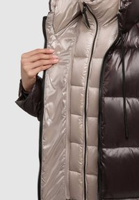 Braune Steppjacke mit Reißverschluss, geöffnet, um das beige satinierte Innenfutter mit gesteppter Polsterung zu zeigen. Reißverschluss mit schwarzem Ziehgriff, sichtbare Strickbündchen.