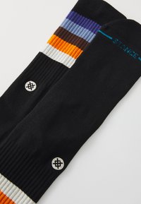 Ciorapi negri până la genunchi cu modele colorate în dungi de purple, albastru, portocaliu și alb. Prezintă un patch cu logo realizat din fir alb pe materialul negru.
