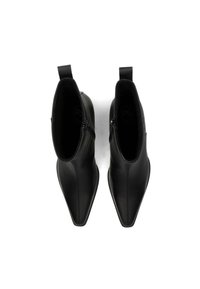 Une paire de bottines en cuir noir avec des bouts pointus et des zips sur le côté, vues de dessus sur un fond blanc.