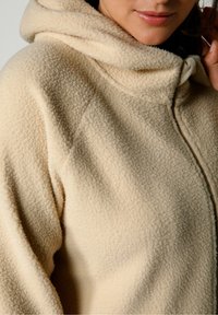 Sudadera de forro polar beige con una superficie suave y texturizada, que presenta un cuello alto y un detalle de cremallera. Sin hardware visible ni patrones.
