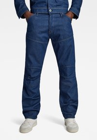 Donkerblauwe denim werkbroek met een relaxte pasvorm. Kenmerken zijn onder meer gestikte details, voorzakken en een knoopsluiting.
