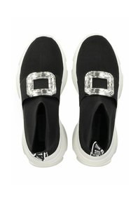 Chaussures noires à enfiler avec une tige en tissu texturé, dotées d'une boucle décorative transparente et d'une semelle en caoutchouc blanche.