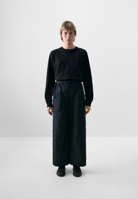 Zwart langemouwen shirt gecombineerd met brede, hoog-getailleerde zwarte broeken. Broeken hebben riemlussen en twee zijzakken.