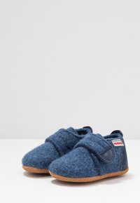 Chaussons en feutre bleu avec une sangle velcro et une semelle en caoutchouc. Design à bout rond et texture douce. Accentué d'une petite étiquette de marque sur le côté.