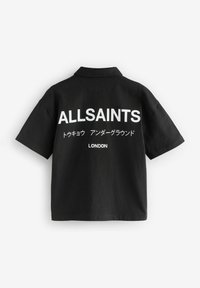 Juoda trumpa rankovėmis marškiniai su apykakle, ant nugaros esantis didelis baltas tekstas: "ALLSAINTS," žemiau papildomas tekstas japonų kalba ir "LONDON."
