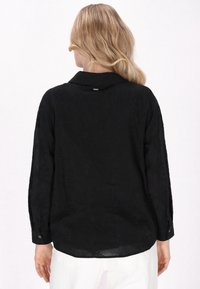 Cămașă neagră cu mâneci lungi, cu un model floral subtil, guler, manșete cu nasturi și tiv rotund, confecționată dintr-un material ușor, texturat.