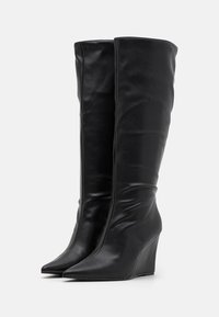 Bottes compensées montantes en cuir noir, avec un bout pointu et une texture plissée, dotées d'une finition lisse et d'une silhouette élégante.