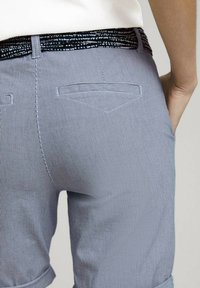 Pantalones a rayas azules con una cinturilla negra estampada, que cuentan con dos bolsillos traseros y un dobladillo enrollado. Textura de tela suave y ligera.
