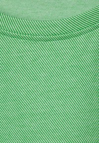 Zelená tkanina s diagonálním pruhovaným vzorem v různých odstínech. Textura se zdá být hladká s jemným pletením a zesíleným švem límce.