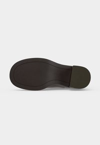Semelle d'une chaussure habillée noire avec une surface lisse légèrement texturée et un talon rectangulaire sur fond blanc.