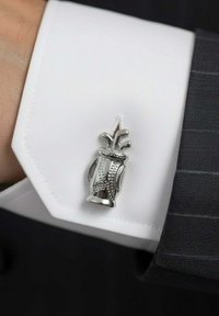 Gemelo de plata con forma de jarrón con detalles decorativos, montado en el puño de una camisa blanca de vestir con bordes definidos.