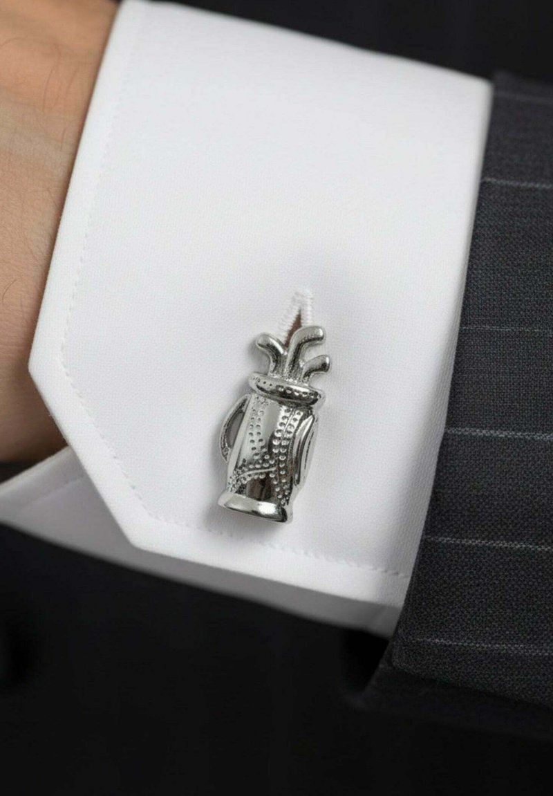 Gemelo de plata con forma de jarrón con detalles decorativos, montado en el puño de una camisa blanca de vestir con bordes definidos.