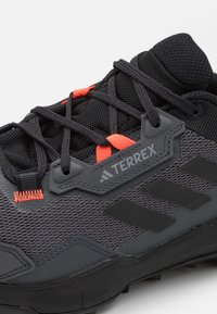 Czarne sportowe buty z siateczkowej cholewki, pomarańczowymi akcentami i teksturowaną podeszwą zapewniającą przyczepność. Marka "TERREX" jest umieszczona na boku.