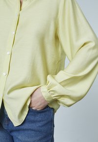 Lys gul button-up skjorte med lange, samlede ærmer; lavet af et blødt stof, parret med blå denim jeans.