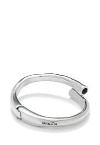 Bracelet en métal argenté au design lisse et arrondi, avec un accent en pierre noire à une extrémité et une marque gravée à l'intérieur.