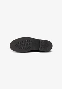 Semelle de chaussure en caoutchouc noir avec des motifs circulaires et une surface texturée pour l'adhérence, avec une marque embossée près du talon.