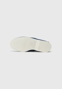 Sötétkék, slip-on stílusú cipő texturált szövet felsőrésszel és fehér gumi talppal. A középtalpon dombornyomott márkajelzés és mintázott talp található.