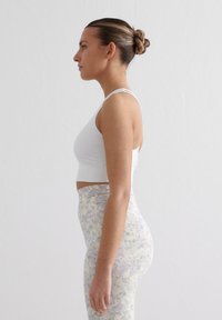 Witte sportbeha met dunne bandjes, gecombineerd met high-waisted leggings met een délicate bloemenpatroon in pastelkleuren.