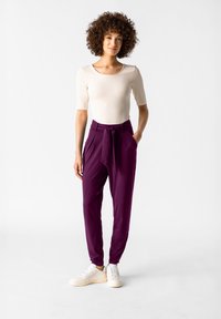 Ljusbeige åtsittande topp med korta ärmar, tillsammans med mörklila högmidjade byxor med knytbälte, bärs med vita sneakers.