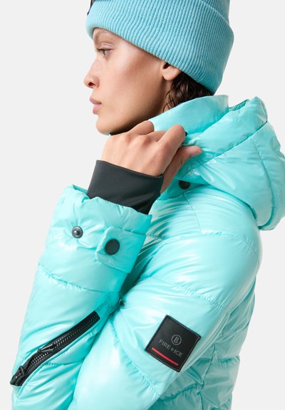 Lichtblauwe gewatteerde jas met een glanzende textuur, ritssluiting, drukknoopsluitingen en zwarte accenten. Draag het met een bijpassende muts.