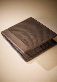 Portefeuille en tissu marron avec une surface texturée, des bords arrondis et plusieurs emplacements pour cartes à l'intérieur. Bordure en cuir le long des bords.