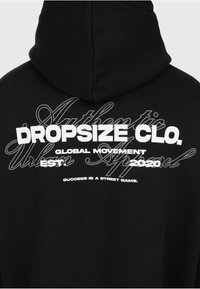 Schwarzer Hoodie-Rückseite mit geschichteten weißen und grauen Texten, die lesen: "Dropsize Clo. Global Movement Est. 2020 Erfolg ist ein Spiel auf der Straße."
