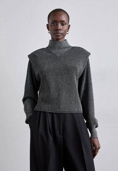 Haut gris texturé avec un col montant, des accents d'épaule et des manches longues ; associé à un pantalon noir ample.