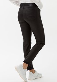 Pantalons ajustés à carreaux noirs avec taille haute et cinq poches, associés à des baskets blanches. Le matériau est lisse avec un léger éclat.