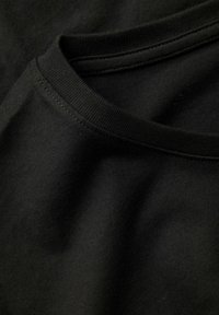 Detailný záber na okrúhly výstrih čierneho trička z bavlny s viditeľným šitím a jemnou textúrou látky.