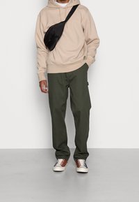 Sudadera con capucha beige, pantalones verde oliva y zapatillas multicolores. Bolso bandolera negro con un diseño texturizado.