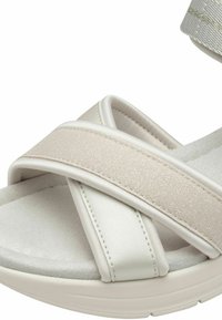 Sandales beige clair avec des brides croisées en matériaux lisses et texturés, semelle rembourrée et une semelle durable légèrement surélevée.