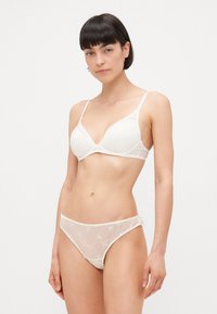 White lace bralette with a soft-cup design and adjustable straps, paired with sheer embroidered panties featuring floral patterns.