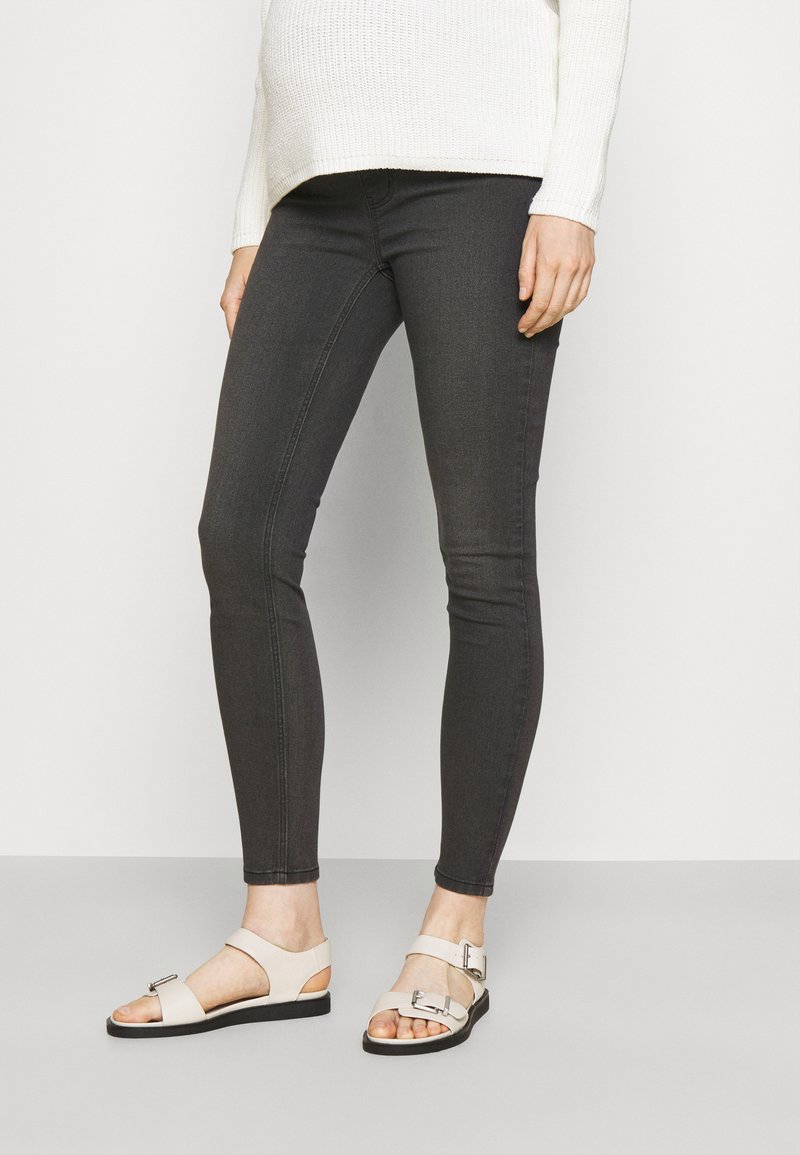 Sandali beige chiaro con suola piatta e dettaglio con fibbia, abbinati a jeans skinny grigi scuri e un maglione bianco a trama.
