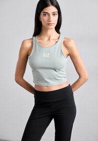 Light green crop top made of stretchy fabric, featuring a round neck and white logo; paired with high-waisted black leggings.