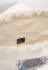 Sac en coton avec un intérieur crème et un imprimé mandala floral à l'extérieur. Comprend une poche zippée et une étiquette avec la marque "even & odd".