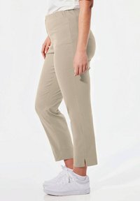 Beige pull-on broek met een slim fit, cropped lengte, zijslitsen aan de zoom, gecombineerd met witte sneakers. Glad stof, geen zichtbare sluitingen.