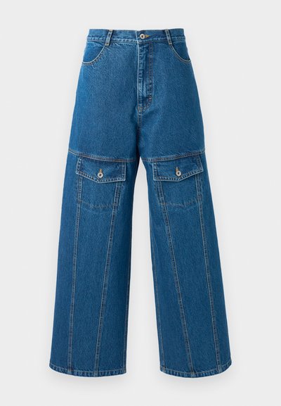 Wide-leg denim trousers in light blue, featuring a high waist, visible stitching, and two buttoned flap pockets on each side.