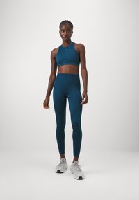 Teal crop top en hoge taille leggings van rekbaar materiaal, met textuurpatronen en een naadloos ontwerp. Grijze sportschoenen.