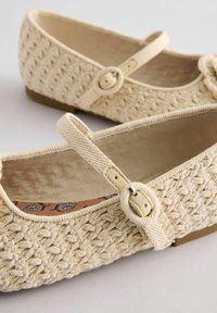 Ballerine intrecciate beige con punta rotonda, suola piatta e una fascia a metà piede con una fibbia rotonda. Tessuto testurizzato e fodera liscia.