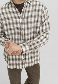 Brun och vit rutig skjorta med knappar, tillverkad av ett strukturerat tyg med klassisk krage och rundad nederkant, med ljusa knappar.